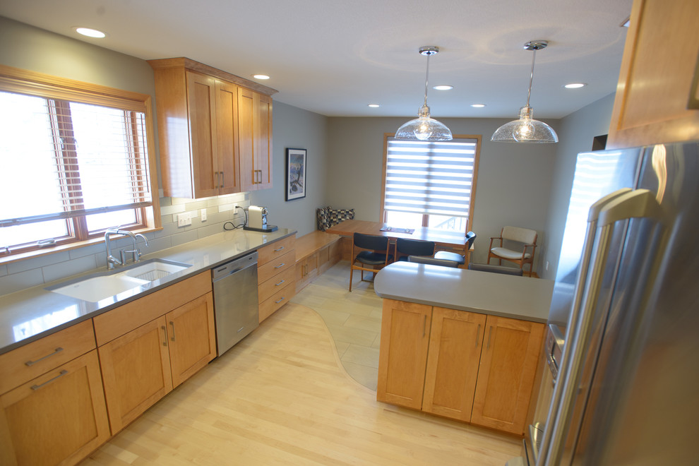 Example of a transitional l-shaped light wood floor kitchen design in Other with an undermount sink, shaker cabinets, light wood cabinets, quartz countertops, gray backsplash, ceramic backsplash, stainless steel appliances and a peninsula