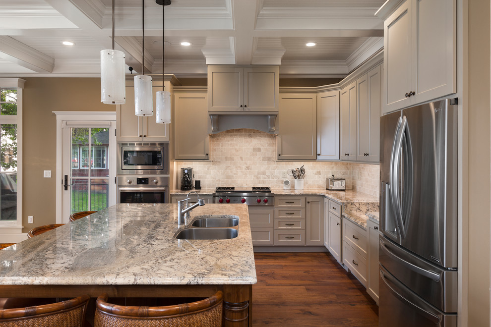 Example of a large transitional l-shaped medium tone wood floor and brown floor open concept kitchen design in Other with an undermount sink, recessed-panel cabinets, gray cabinets, granite countertops, beige backsplash, stone tile backsplash, stainless steel appliances, an island and multicolored countertops