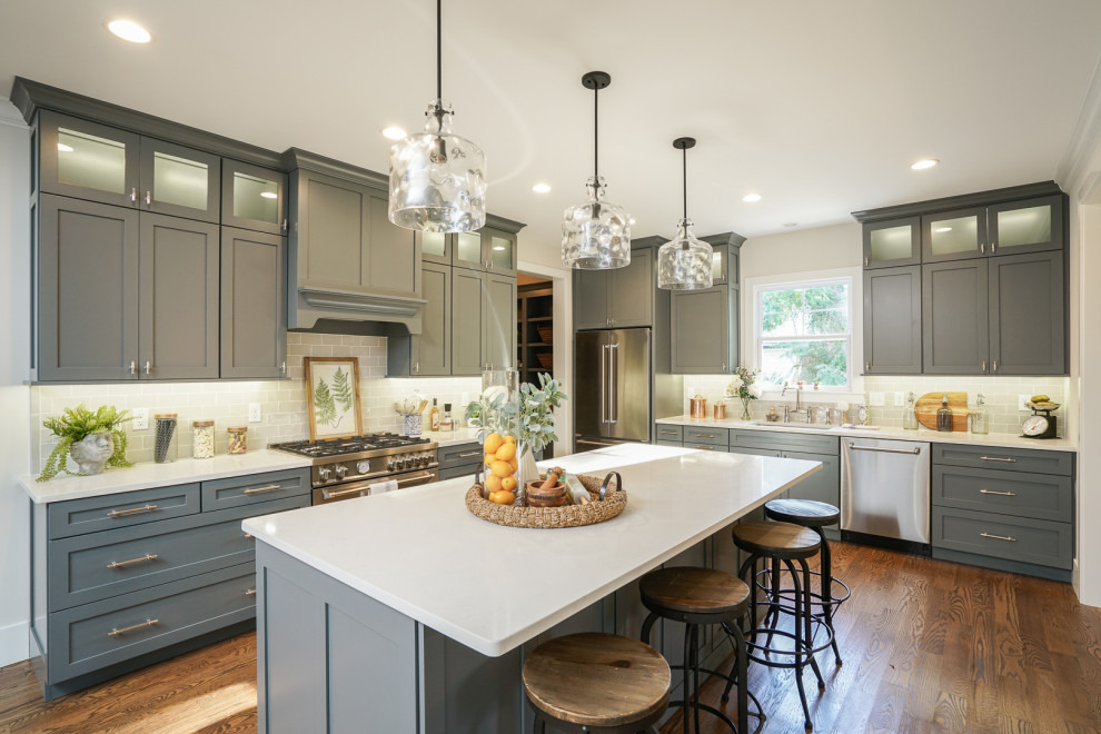 Inspiration for a transitional l-shaped dark wood floor and brown floor kitchen remodel in St Louis with an undermount sink, shaker cabinets, gray cabinets, gray backsplash, subway tile backsplash, stainless steel appliances, an island and white countertops