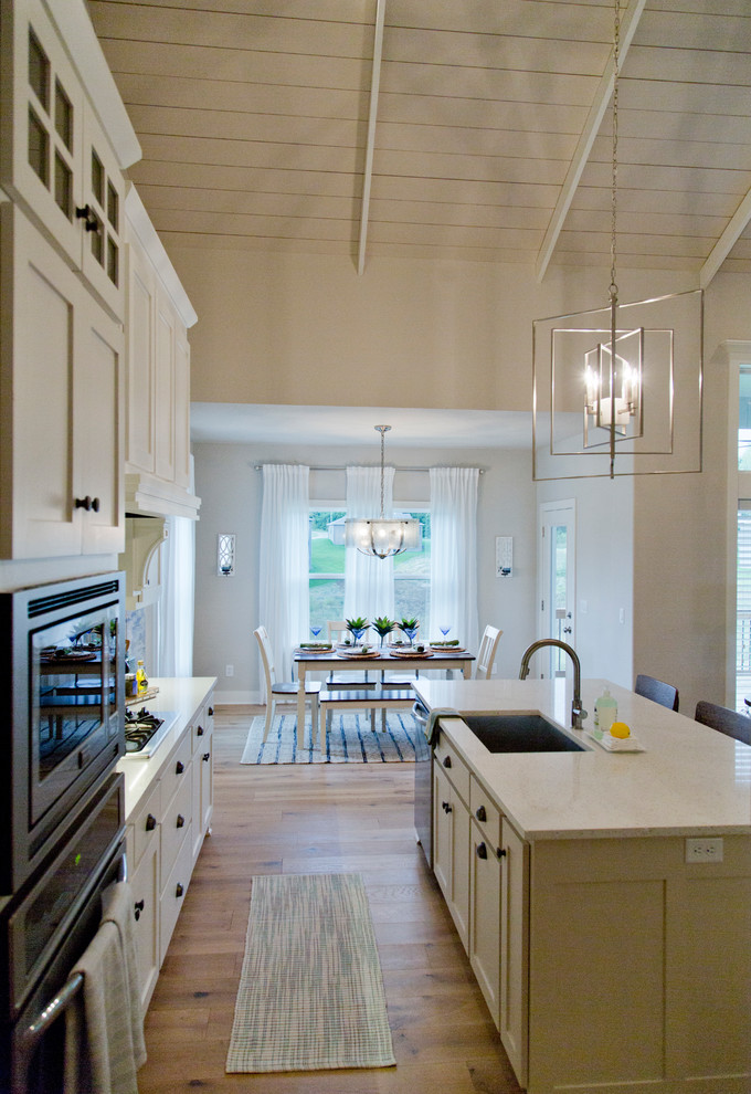 Exempel på ett stort maritimt kök, med en undermonterad diskho, luckor med glaspanel, vita skåp, grått stänkskydd, stänkskydd i keramik, rostfria vitvaror, ljust trägolv, en köksö och brunt golv