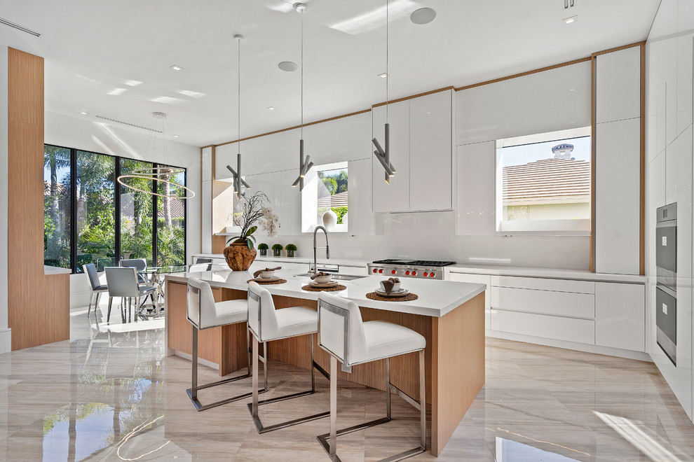 Moderne Wohnküche in L-Form mit Unterbauwaschbecken, flächenbündigen Schrankfronten, weißen Schränken, Küchenrückwand in Weiß, Küchengeräten aus Edelstahl, Kücheninsel, beigem Boden und weißer Arbeitsplatte in Miami