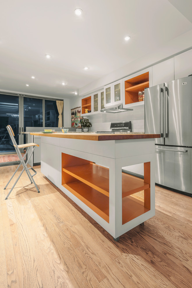 Medium sized contemporary galley enclosed kitchen in Toronto with a submerged sink, flat-panel cabinets, white cabinets, wood worktops, white splashback, ceramic splashback, stainless steel appliances, medium hardwood flooring, an island, brown floors and brown worktops.