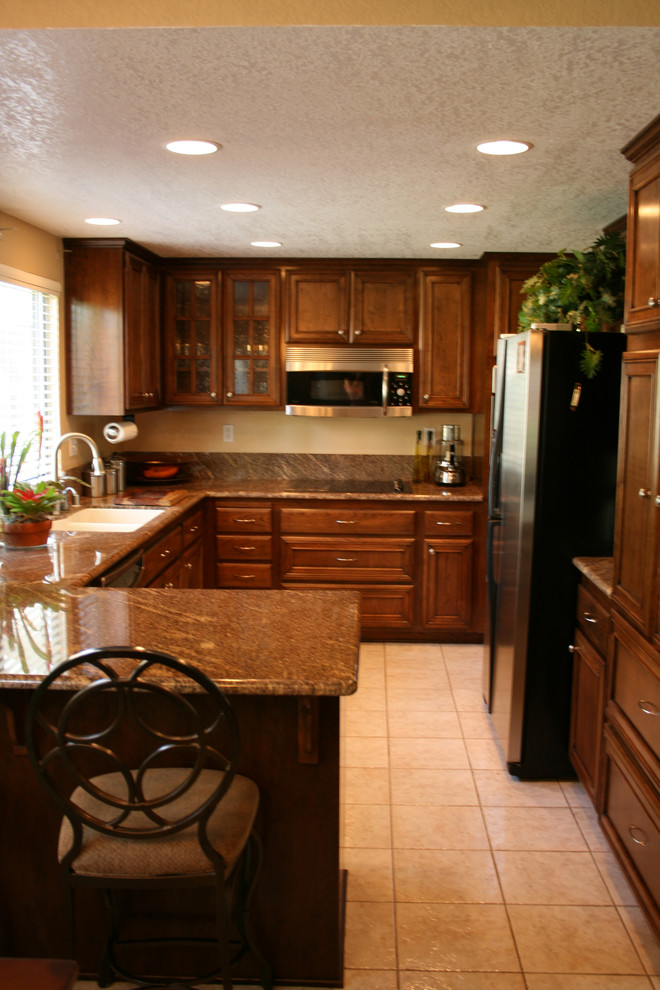Foto på ett avskilt, mellanstort vintage u-kök, med en undermonterad diskho, luckor med infälld panel, skåp i mörkt trä, granitbänkskiva, brunt stänkskydd, stänkskydd i stenkakel och rostfria vitvaror