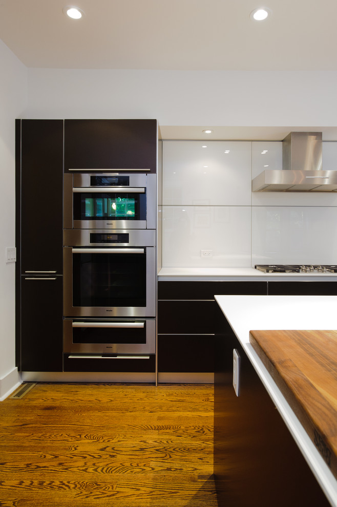 Exempel på ett modernt kök, med en undermonterad diskho, släta luckor, bruna skåp, laminatbänkskiva, gult stänkskydd, glaspanel som stänkskydd, rostfria vitvaror, mellanmörkt trägolv och en köksö