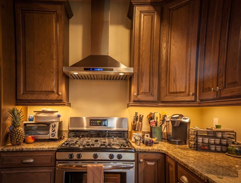 Exemple d'une cuisine américaine parallèle montagne en bois foncé de taille moyenne avec un plan de travail en granite, une crédence beige, un électroménager en acier inoxydable, parquet clair et îlot.