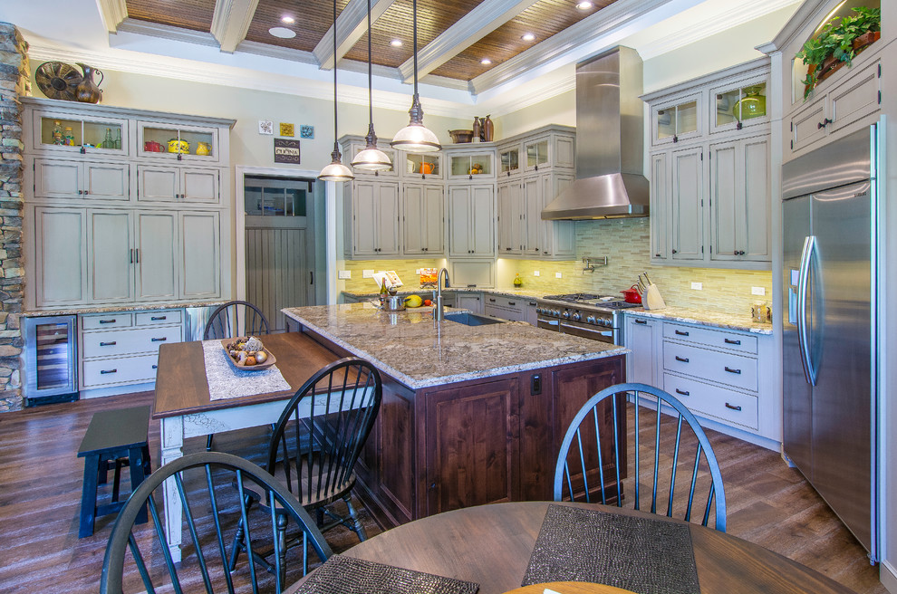 Inspiration for an expansive traditional u-shaped open plan kitchen in Tampa with a belfast sink, beaded cabinets, beige cabinets, granite worktops, beige splashback, mosaic tiled splashback, stainless steel appliances, medium hardwood flooring, an island and brown floors.
