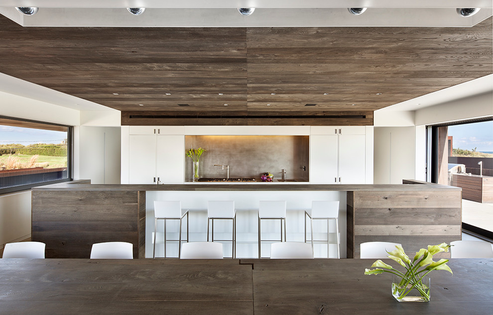 This is an example of a contemporary galley kitchen/diner in New York with flat-panel cabinets, white cabinets and an island.