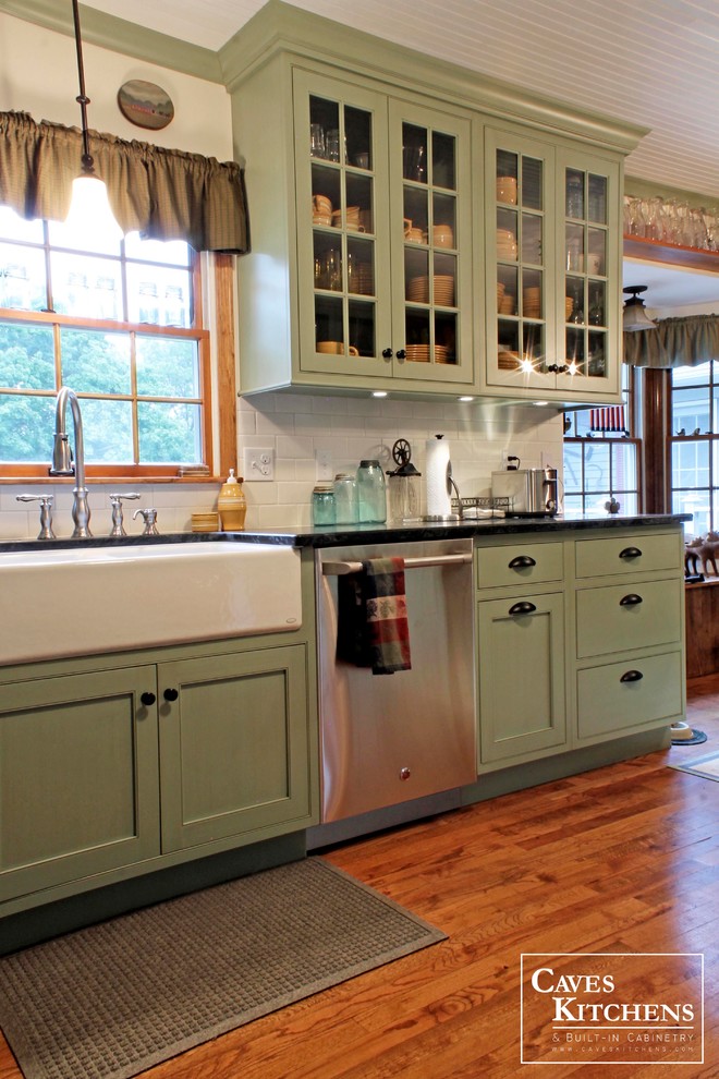 Example of a mid-sized transitional u-shaped medium tone wood floor eat-in kitchen design in New York with a farmhouse sink, glass-front cabinets, green cabinets, soapstone countertops, subway tile backsplash, stainless steel appliances, white backsplash and no island