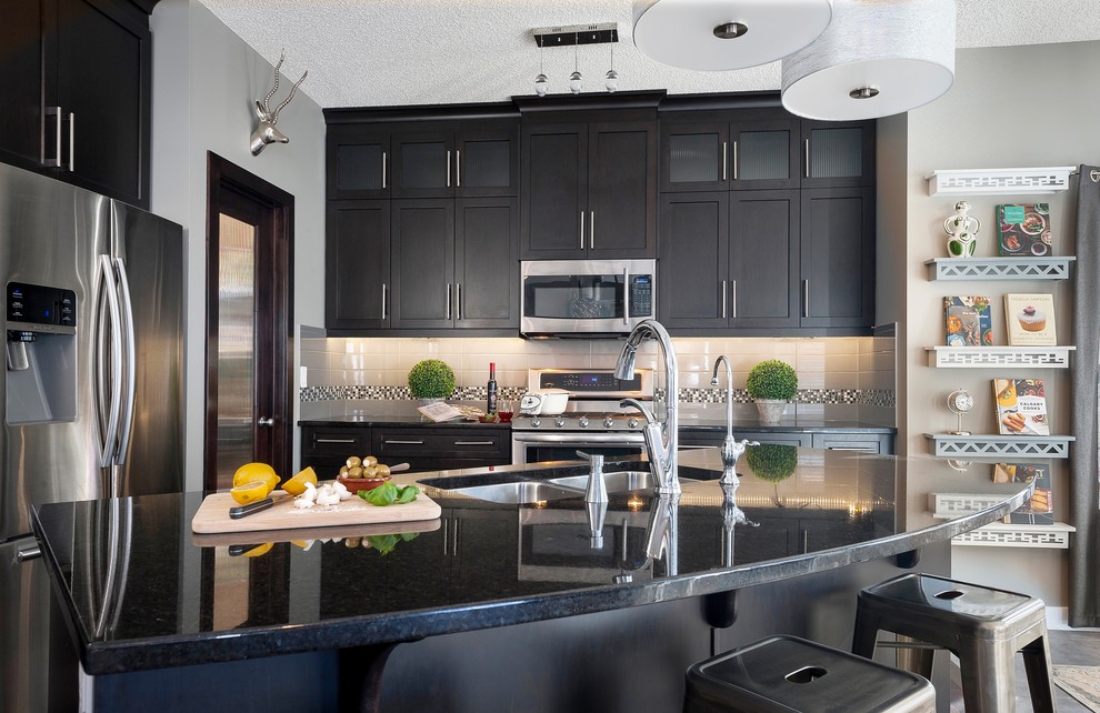 This is an example of a contemporary l-shaped kitchen in Calgary with a double-bowl sink, glass-front cabinets, dark wood cabinets, granite worktops, grey splashback, metro tiled splashback, stainless steel appliances, dark hardwood flooring and an island.