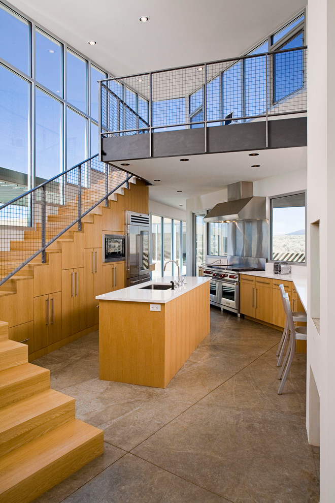 Modern inredning av ett kök, med en undermonterad diskho, släta luckor, skåp i ljust trä, stänkskydd med metallisk yta, stänkskydd i metallkakel och rostfria vitvaror