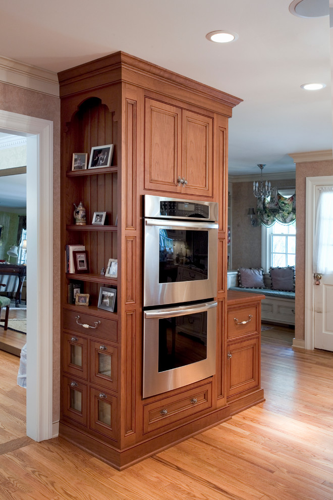 Diseño de cocina clásica con puertas de armario de madera oscura, electrodomésticos de acero inoxidable y suelo de madera en tonos medios