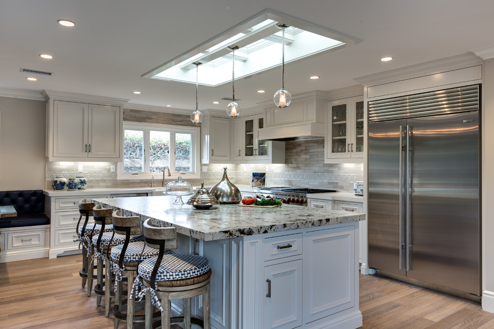 Large transitional l-shaped light wood floor and beige floor eat-in kitchen photo in Orange County with white cabinets, solid surface countertops, gray backsplash, stone tile backsplash, stainless steel appliances, a farmhouse sink, an island and recessed-panel cabinets