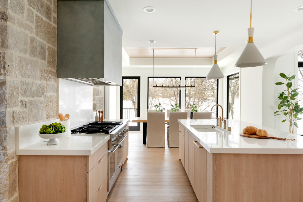 Diseño de cocina comedor nórdica con puertas de armario de madera clara, encimera de cuarcita, electrodomésticos de acero inoxidable, suelo de madera clara y encimeras blancas