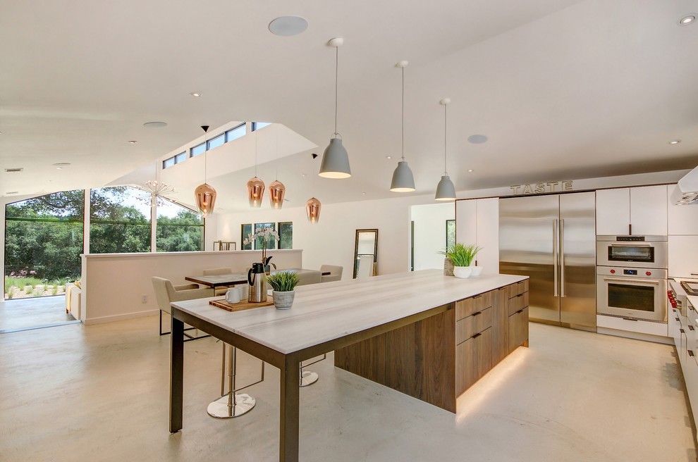 Photo of a farmhouse l-shaped kitchen/diner in San Francisco with a belfast sink, flat-panel cabinets, white cabinets, marble worktops, stainless steel appliances, concrete flooring, an island, grey floors and white worktops.