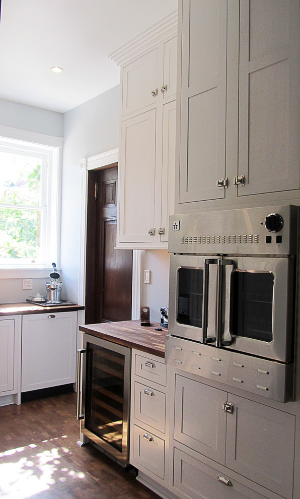 Cette image montre une cuisine ouverte linéaire de taille moyenne avec un placard avec porte à panneau encastré, des portes de placard blanches, un plan de travail en bois, un électroménager en acier inoxydable, un sol en bois brun et un sol marron.