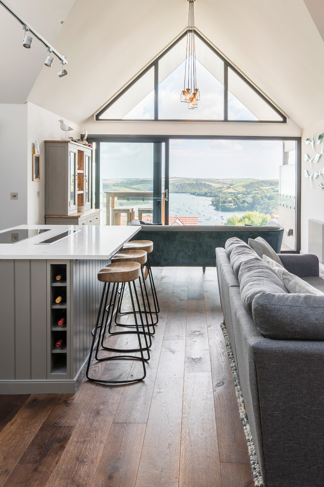 Inspiration for a large modern l-shaped open plan kitchen in Devon with a belfast sink, shaker cabinets, grey cabinets, composite countertops, light hardwood flooring and an island.