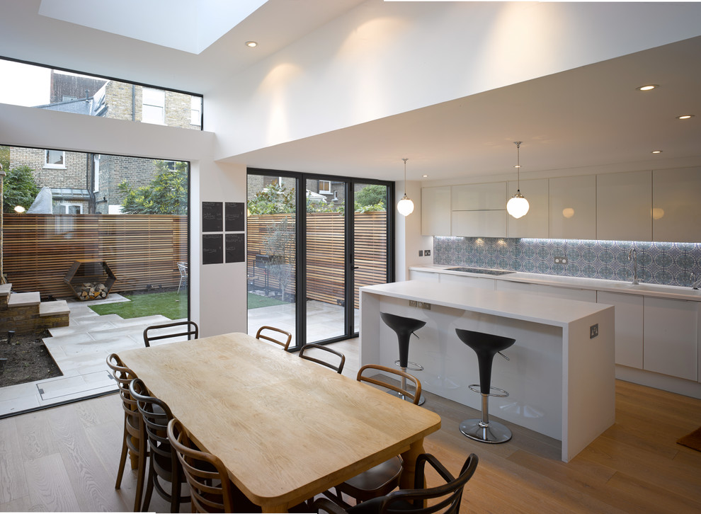 Zweizeilige, Große Moderne Wohnküche mit flächenbündigen Schrankfronten, weißen Schränken, Küchenrückwand in Weiß, hellem Holzboden, Kücheninsel und braunem Boden in London