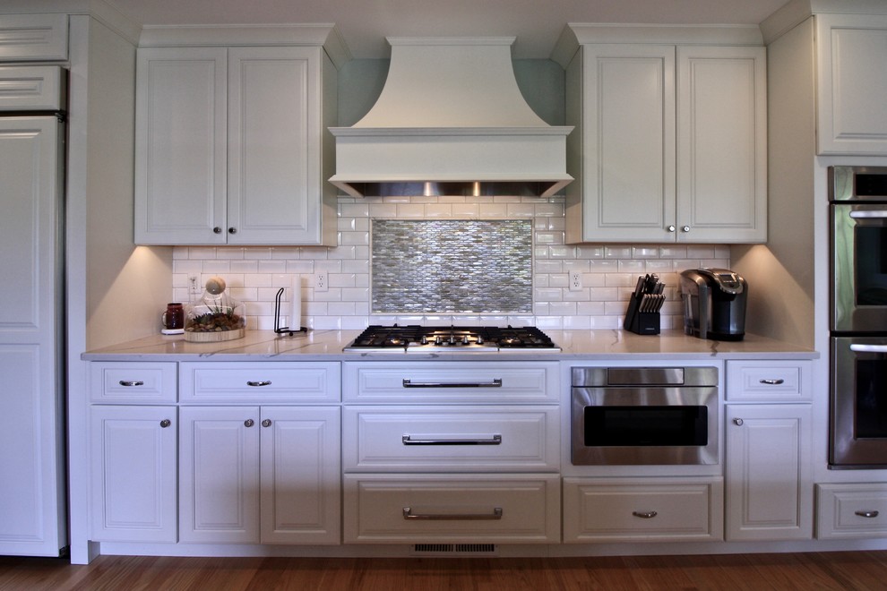 Example of a large transitional single-wall light wood floor open concept kitchen design in St Louis with a drop-in sink, raised-panel cabinets, white cabinets, quartz countertops, white backsplash, ceramic backsplash, paneled appliances and two islands
