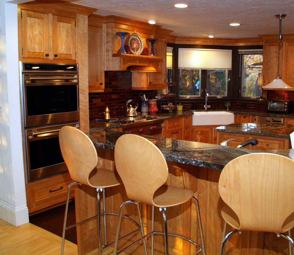 Bild på ett stort rustikt kök, med en rustik diskho, luckor med infälld panel, skåp i mellenmörkt trä, granitbänkskiva, rött stänkskydd, stänkskydd i tegel, rostfria vitvaror, ljust trägolv och flera köksöar