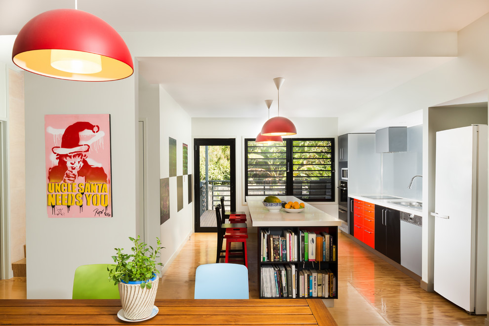 Modelo de cocina comedor lineal contemporánea con armarios con paneles lisos, salpicadero azul, suelo de madera en tonos medios y una isla