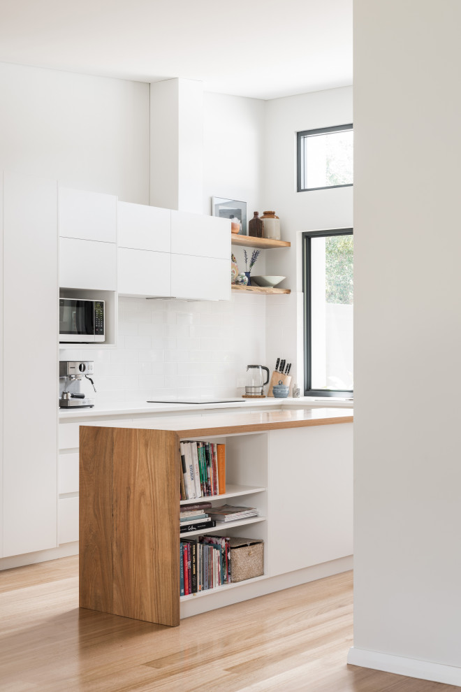 Contemporary l-shaped kitchen in Other with flat-panel cabinets, white cabinets, wood worktops, white splashback, light hardwood flooring, an island, beige floors, brown worktops and a vaulted ceiling.