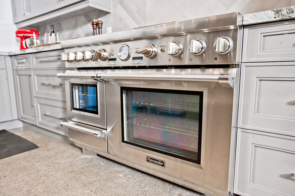 Foto på ett stort funkis kök, med en nedsänkt diskho, luckor med infälld panel, grå skåp, granitbänkskiva, grått stänkskydd, stänkskydd i stenkakel, rostfria vitvaror, betonggolv och en halv köksö