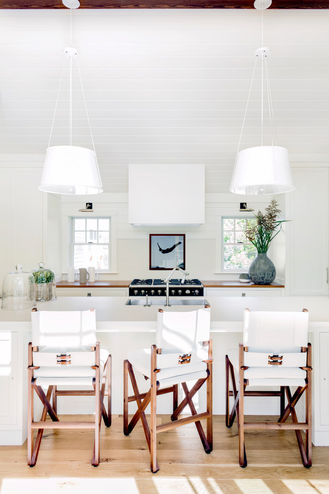 Cette photo montre une cuisine ouverte chic avec un évier encastré, un placard à porte shaker, des portes de placard blanches, un plan de travail en bois, une crédence blanche, un électroménager noir, parquet clair et îlot.