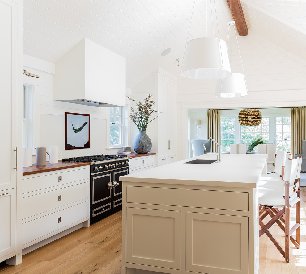 Inspiration for a traditional open plan kitchen in Boston with a submerged sink, shaker cabinets, white cabinets, wood worktops, white splashback, black appliances, light hardwood flooring and an island.