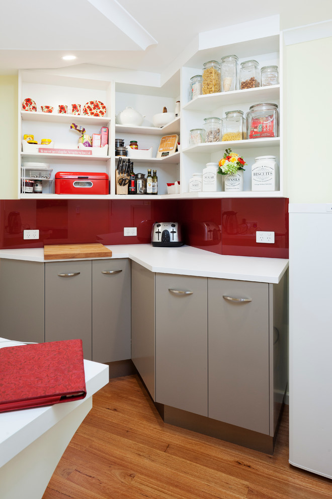 Moderne Küche mit flächenbündigen Schrankfronten, beigen Schränken, Quarzwerkstein-Arbeitsplatte, Küchenrückwand in Rot, Glasrückwand und weißer Arbeitsplatte in Perth