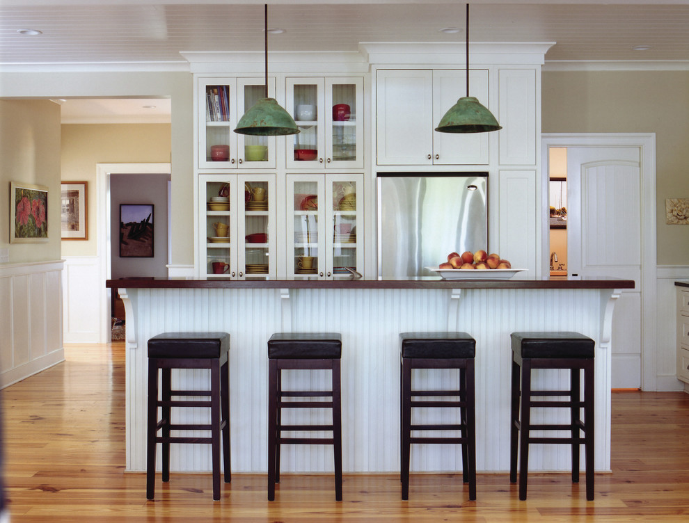 Photo of a beach style l-shaped kitchen/diner in Charleston with glass-front cabinets, white cabinets, stainless steel appliances, light hardwood flooring and an island.