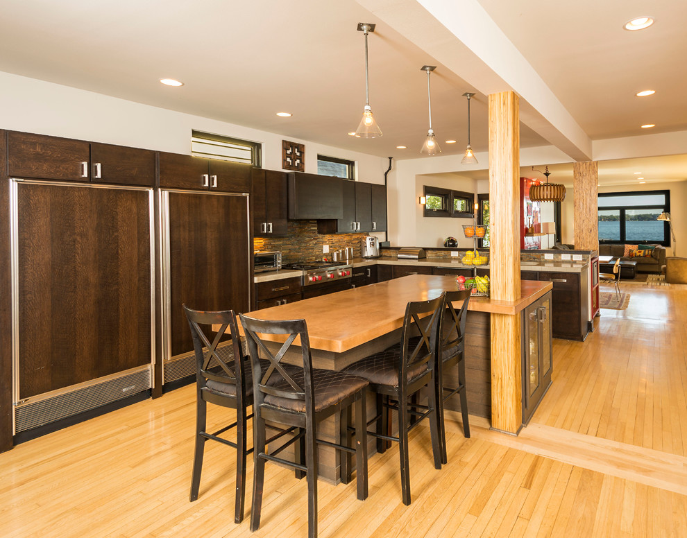 Example of a large urban l-shaped light wood floor open concept kitchen design in Other with shaker cabinets, dark wood cabinets, granite countertops, brown backsplash, mosaic tile backsplash, paneled appliances and an island