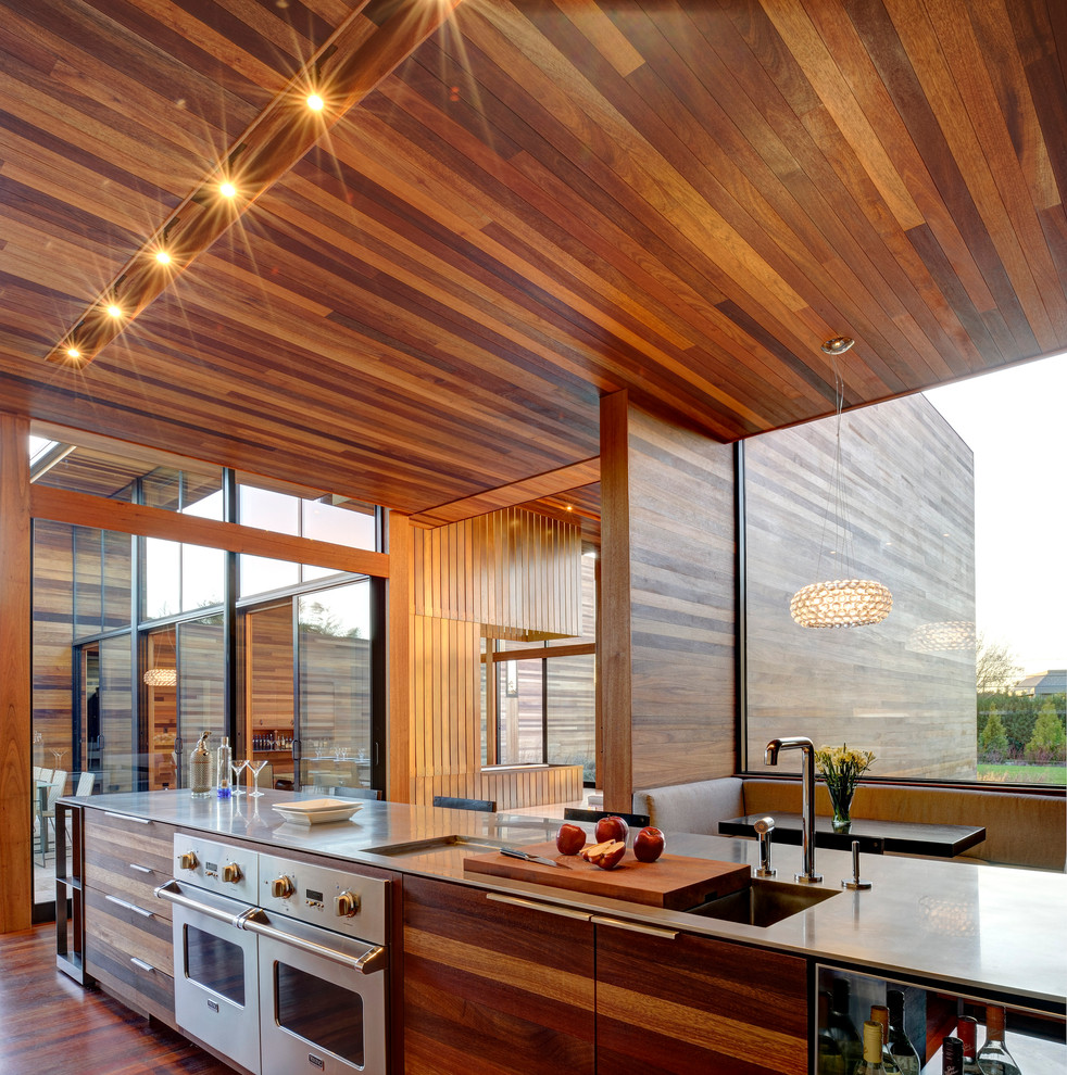 Modelo de cocina comedor actual con armarios con paneles lisos, fregadero integrado, electrodomésticos de acero inoxidable y puertas de armario de madera oscura