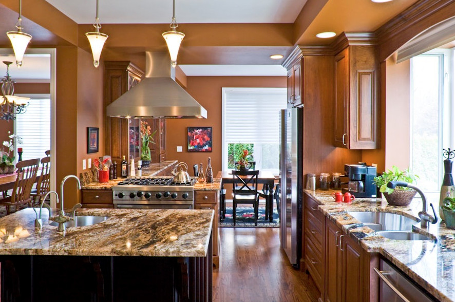 Einzeilige, Mittelgroße Klassische Wohnküche mit Granit-Arbeitsplatte, zwei Kücheninseln, Doppelwaschbecken, profilierten Schrankfronten, hellen Holzschränken, Küchengeräten aus Edelstahl und braunem Holzboden in Seattle