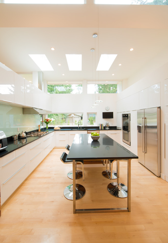 Exempel på ett mellanstort modernt kök, med släta luckor, glaspanel som stänkskydd, rostfria vitvaror, en undermonterad diskho, gula skåp, granitbänkskiva, grönt stänkskydd, ljust trägolv och en köksö
