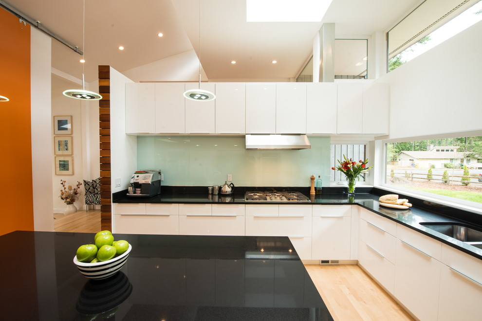 Modern inredning av ett mellanstort kök, med en undermonterad diskho, släta luckor, gula skåp, granitbänkskiva, grönt stänkskydd, glaspanel som stänkskydd, rostfria vitvaror, ljust trägolv och en köksö