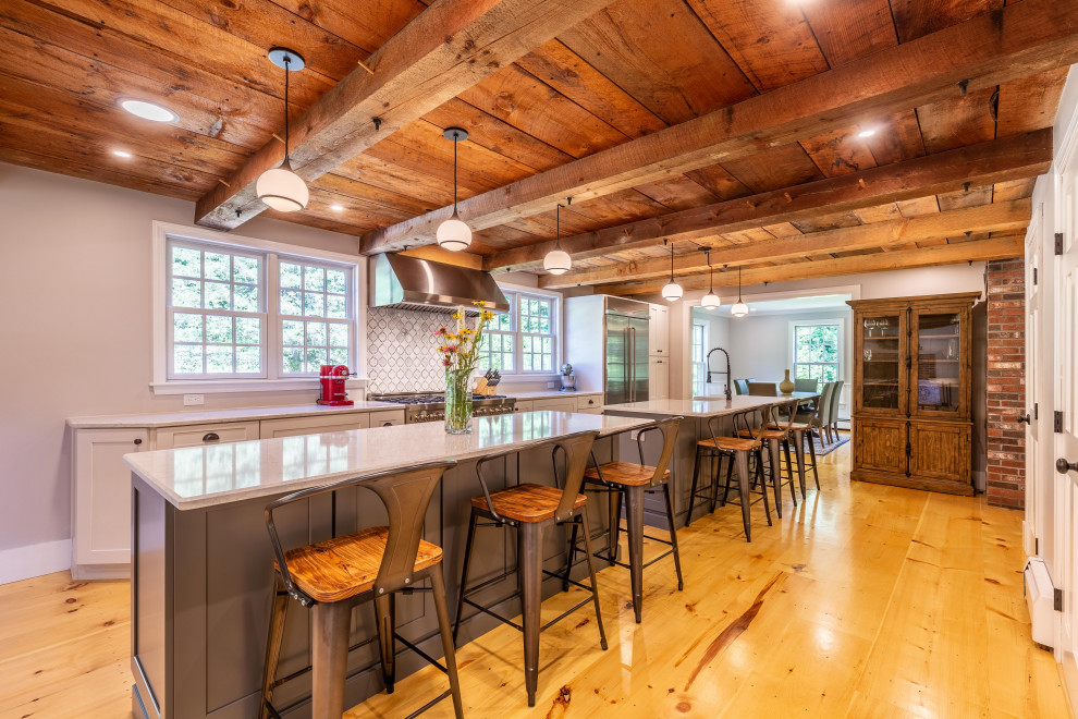 Inspiration for a farmhouse galley medium tone wood floor, brown floor and wood ceiling kitchen remodel in Boston with a farmhouse sink, shaker cabinets, white cabinets, stainless steel appliances, two islands and white countertops