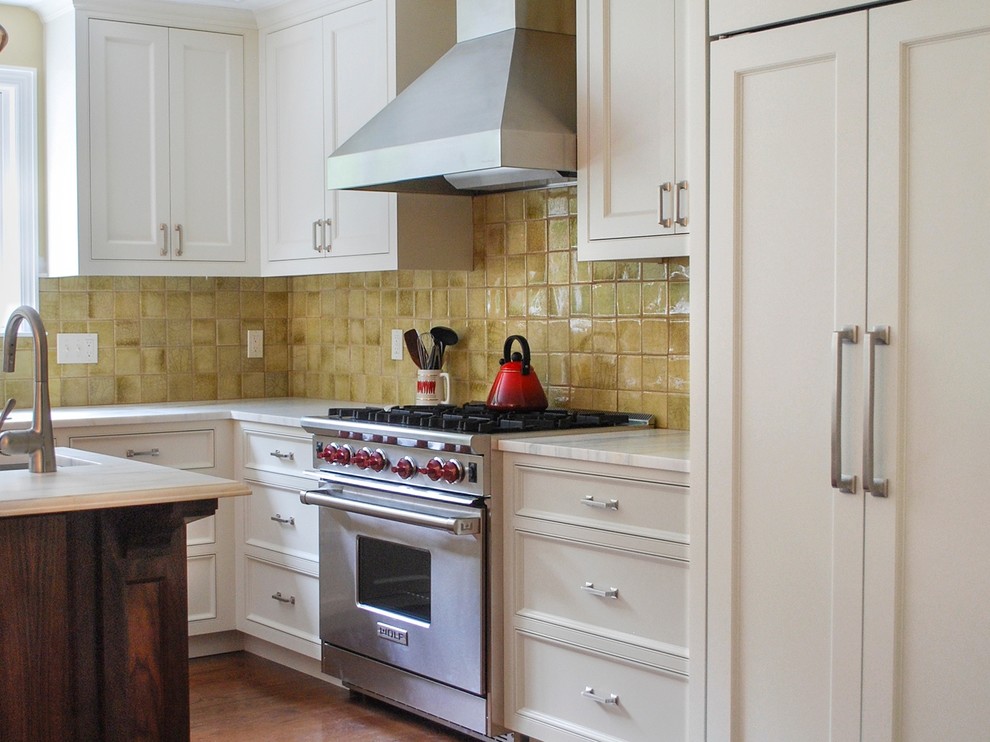 This is an example of a traditional l-shaped kitchen in New York with a submerged sink, recessed-panel cabinets, white cabinets, yellow splashback, glass tiled splashback, stainless steel appliances, medium hardwood flooring and an island.