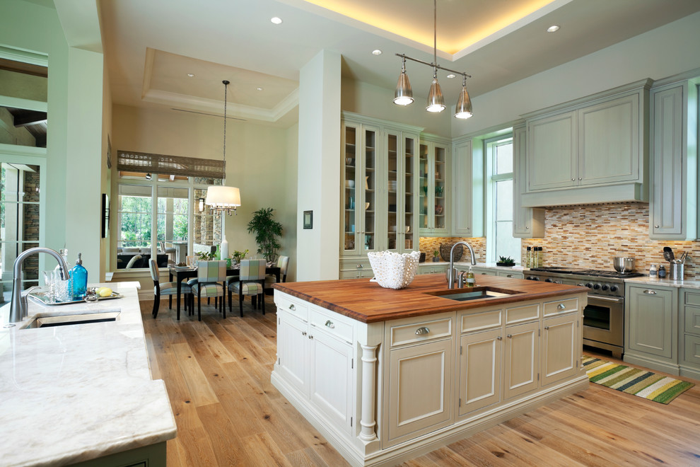 Klassisk inredning av ett kök och matrum, med en undermonterad diskho, luckor med infälld panel, gröna skåp, flerfärgad stänkskydd, stänkskydd i mosaik, rostfria vitvaror och träbänkskiva