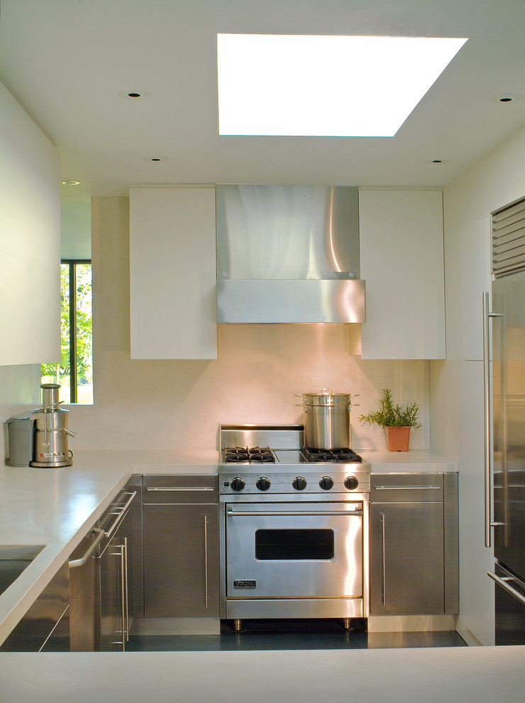 Foto di una piccola cucina ad U design con lavello sottopiano, ante lisce, ante in acciaio inossidabile, paraspruzzi bianco e penisola