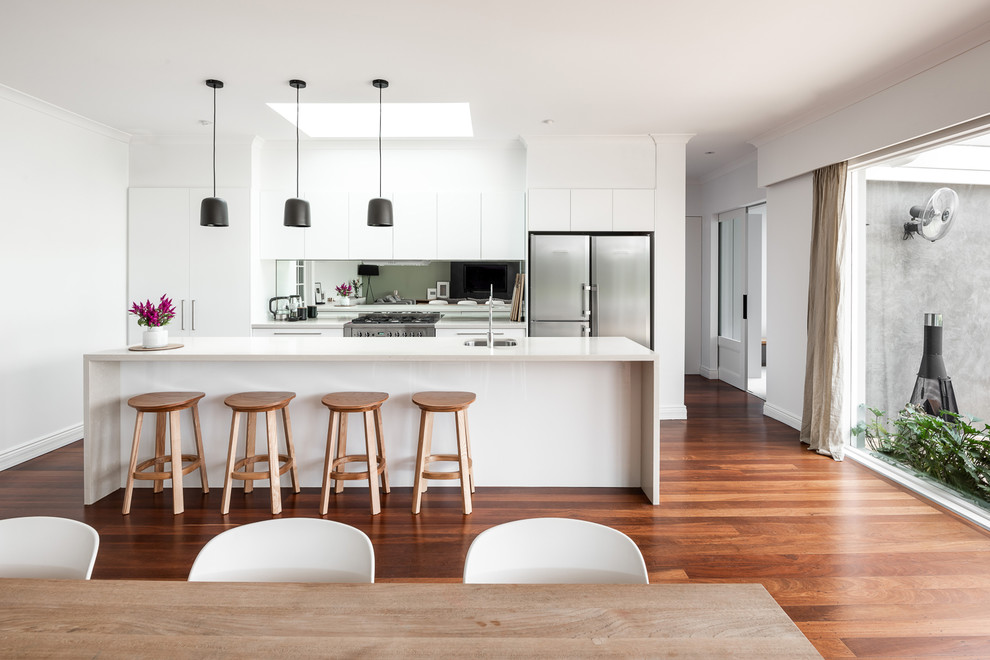 Medium sized contemporary single-wall kitchen/diner in Perth with raised-panel cabinets, white cabinets, engineered stone countertops, mirror splashback, an island, white worktops, a submerged sink, metallic splashback, stainless steel appliances, dark hardwood flooring and brown floors.