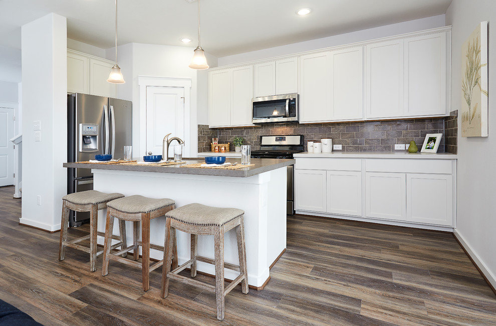 Mid-sized trendy l-shaped medium tone wood floor and brown floor kitchen photo in Dallas with an undermount sink, recessed-panel cabinets, white cabinets, solid surface countertops, brown backsplash, ceramic backsplash, stainless steel appliances, an island and beige countertops