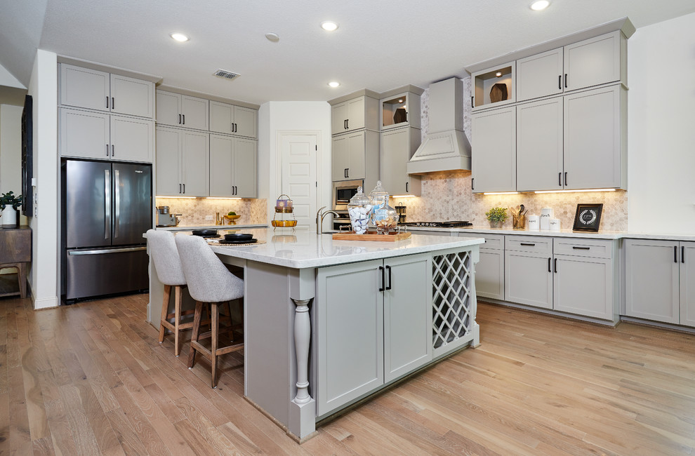 Medium sized traditional l-shaped kitchen/diner in Other with a submerged sink, recessed-panel cabinets, grey cabinets, composite countertops, beige splashback, stainless steel appliances, light hardwood flooring, an island, beige floors and white worktops.