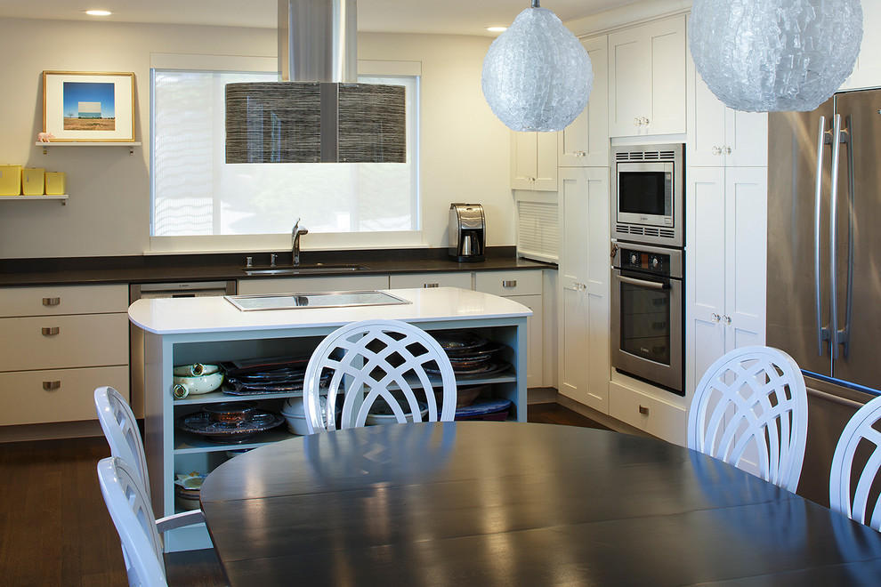 Modern inredning av ett mellanstort kök, med en dubbel diskho, släta luckor, vita skåp, bänkskiva i kvarts, svart stänkskydd, rostfria vitvaror, mörkt trägolv, en köksö och brunt golv
