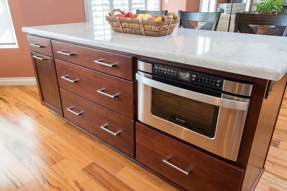 Photo of a medium sized modern single-wall kitchen/diner in San Diego with a built-in sink, shaker cabinets, medium wood cabinets, engineered stone countertops, white splashback, ceramic splashback, stainless steel appliances, medium hardwood flooring and an island.