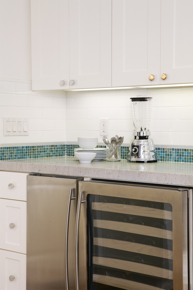 Modelo de cocina clásica con armarios estilo shaker, puertas de armario blancas, encimera de cuarzo compacto, salpicadero azul, salpicadero con mosaicos de azulejos y electrodomésticos de acero inoxidable