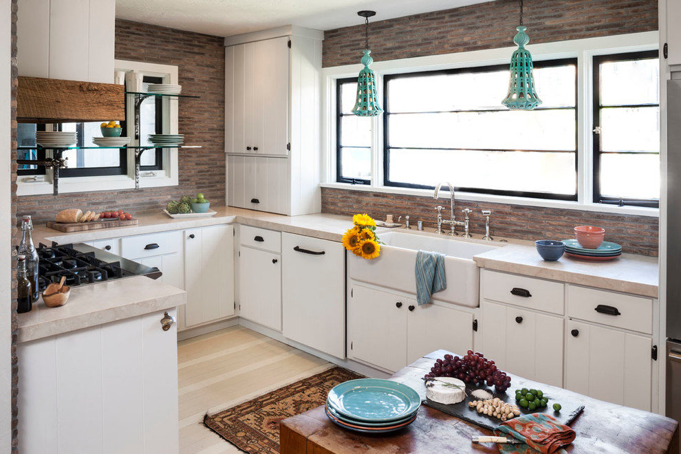Design ideas for a bohemian u-shaped enclosed kitchen in Orange County with a belfast sink, flat-panel cabinets, white cabinets, stainless steel appliances and marble worktops.