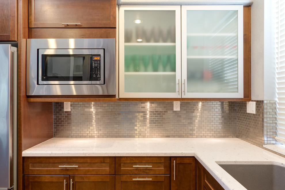Inredning av ett modernt mellanstort kök, med en dubbel diskho, luckor med infälld panel, skåp i mellenmörkt trä, bänkskiva i kvartsit, stänkskydd med metallisk yta, spegel som stänkskydd, rostfria vitvaror, ljust trägolv och en köksö
