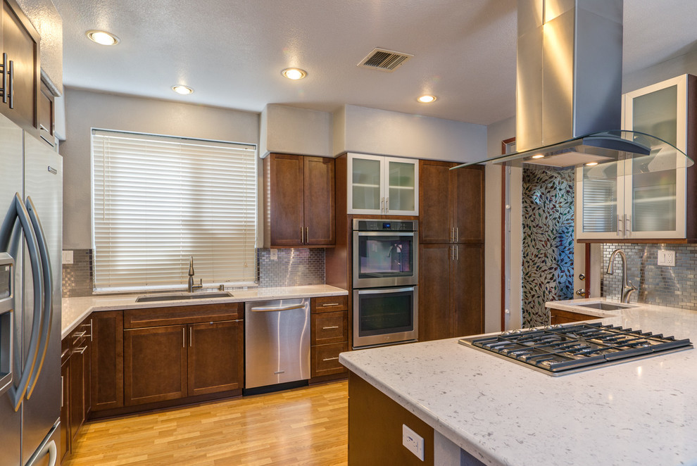 Mid-sized trendy l-shaped light wood floor eat-in kitchen photo in San Diego with a double-bowl sink, recessed-panel cabinets, medium tone wood cabinets, quartzite countertops, metallic backsplash, mirror backsplash, stainless steel appliances and an island