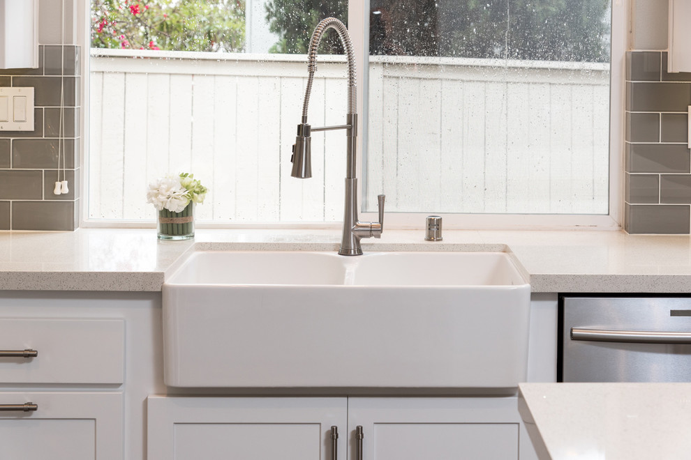 Example of a mid-sized minimalist u-shaped kitchen design in San Diego with a farmhouse sink, shaker cabinets, white cabinets, quartz countertops, gray backsplash, subway tile backsplash, stainless steel appliances and an island