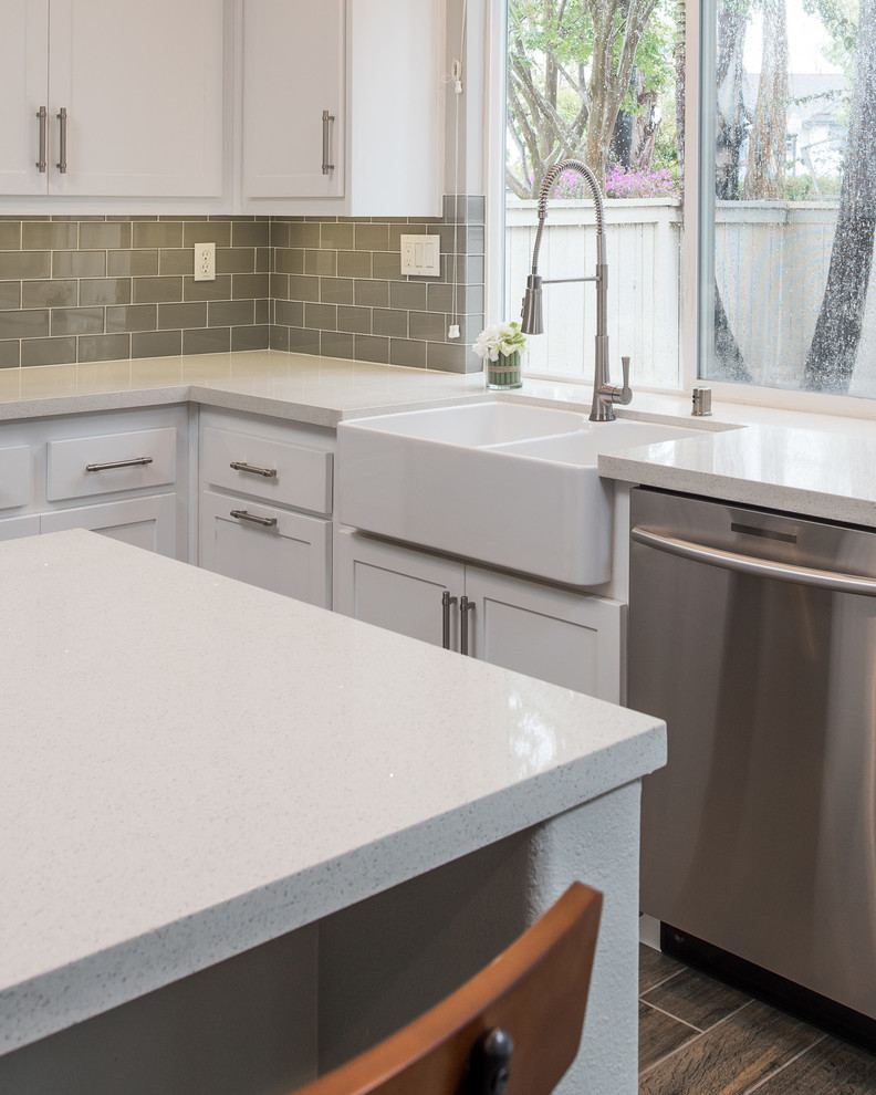 This is an example of a medium sized modern u-shaped kitchen in San Diego with a belfast sink, shaker cabinets, white cabinets, engineered stone countertops, grey splashback, metro tiled splashback, stainless steel appliances, plywood flooring and an island.